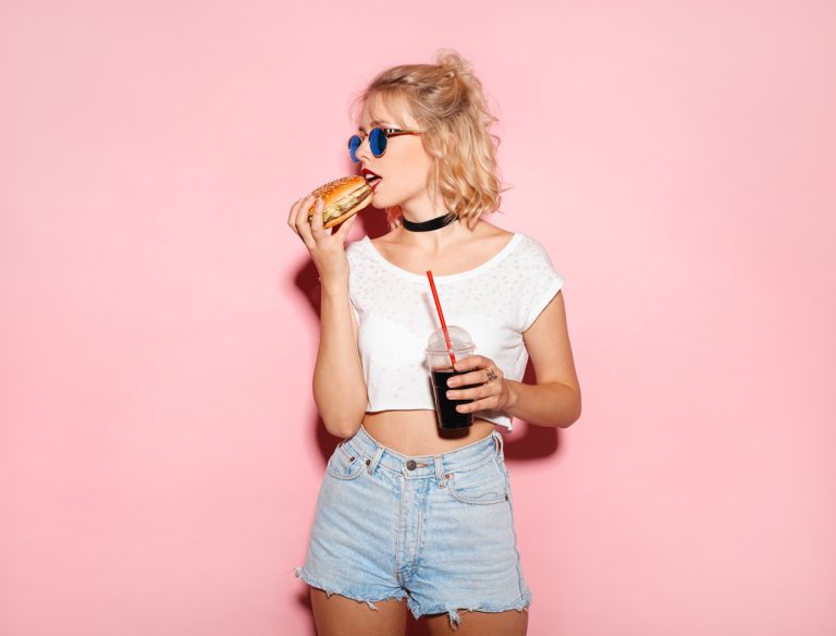 girl eating a burger with soda in hand