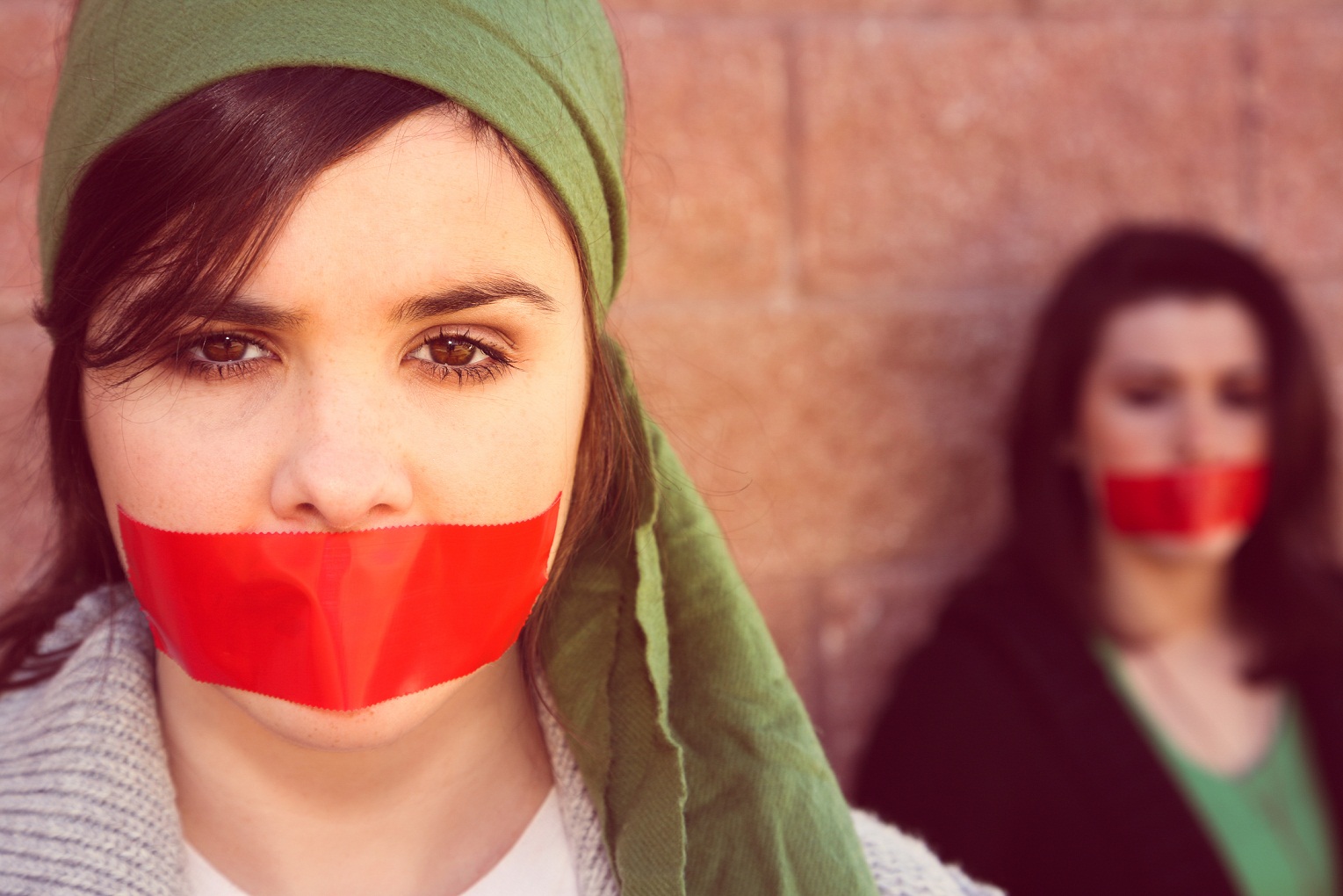 two women with red tape across their mouths