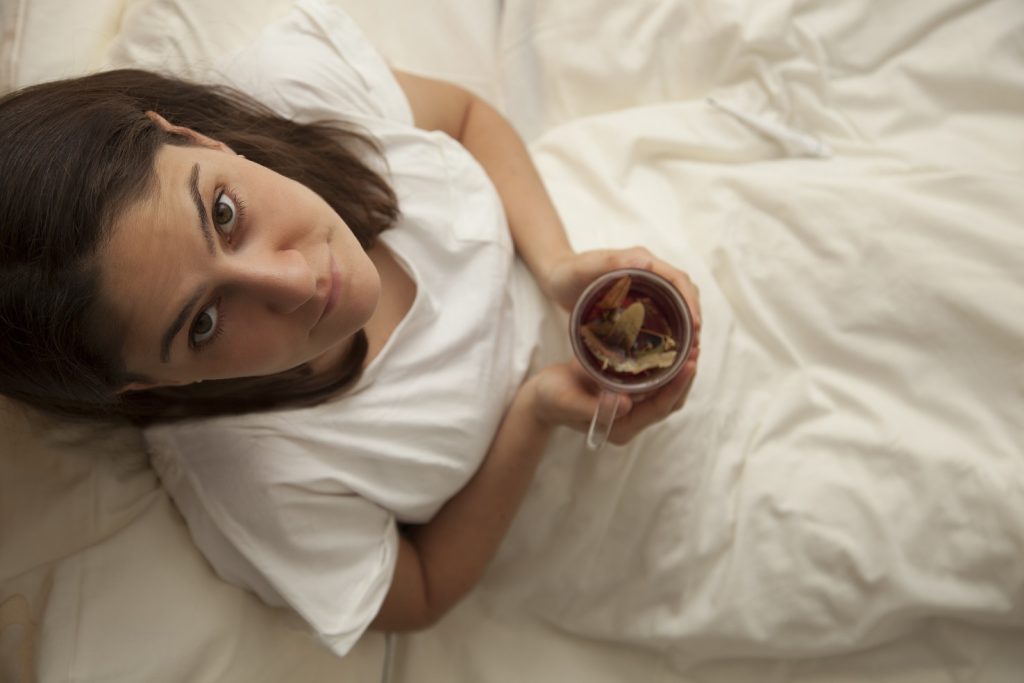 woman laying in bed with cup of hot tea