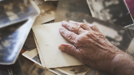 hand of elderly person over old photos Quest for Alzheimer’s Vaccine Hitting Roadblocks