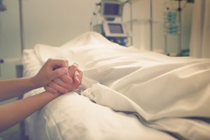 woman holding hand of dead husband in hospital