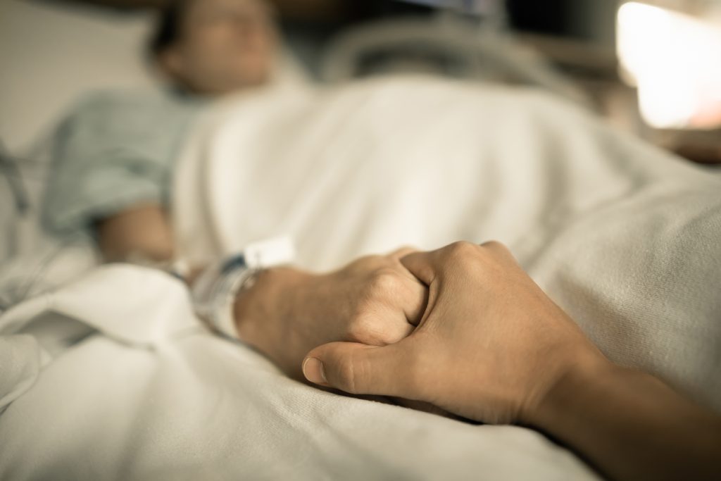 holding hand of man in hospital bed